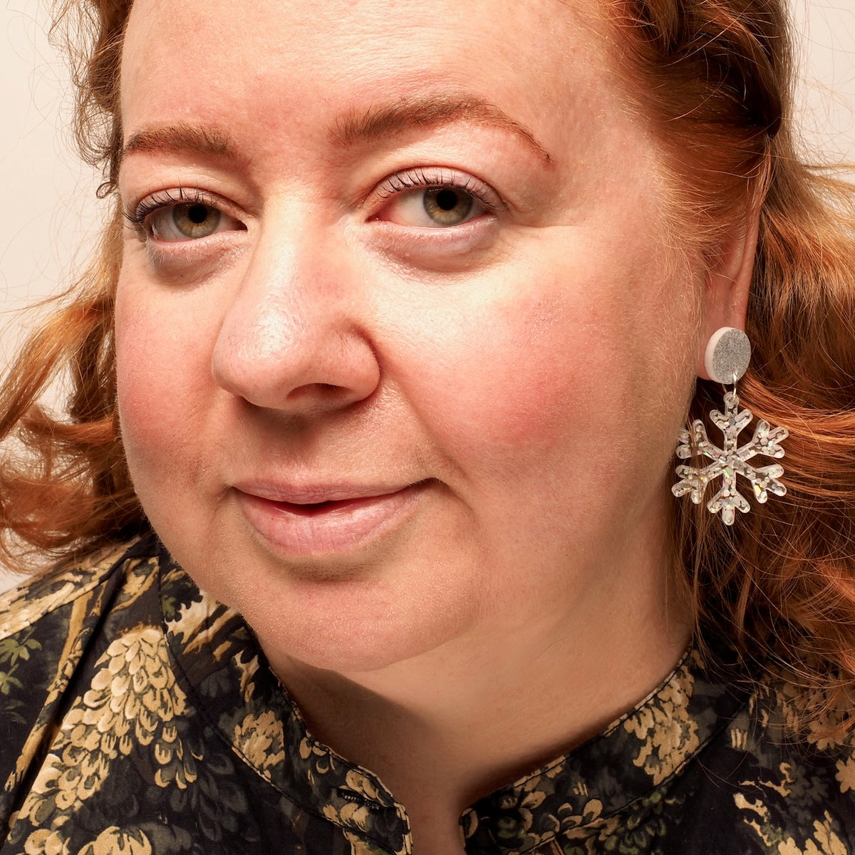 Close-up portrait of a woman with red hair wearing a silver snowflake-shaped  drop earring.