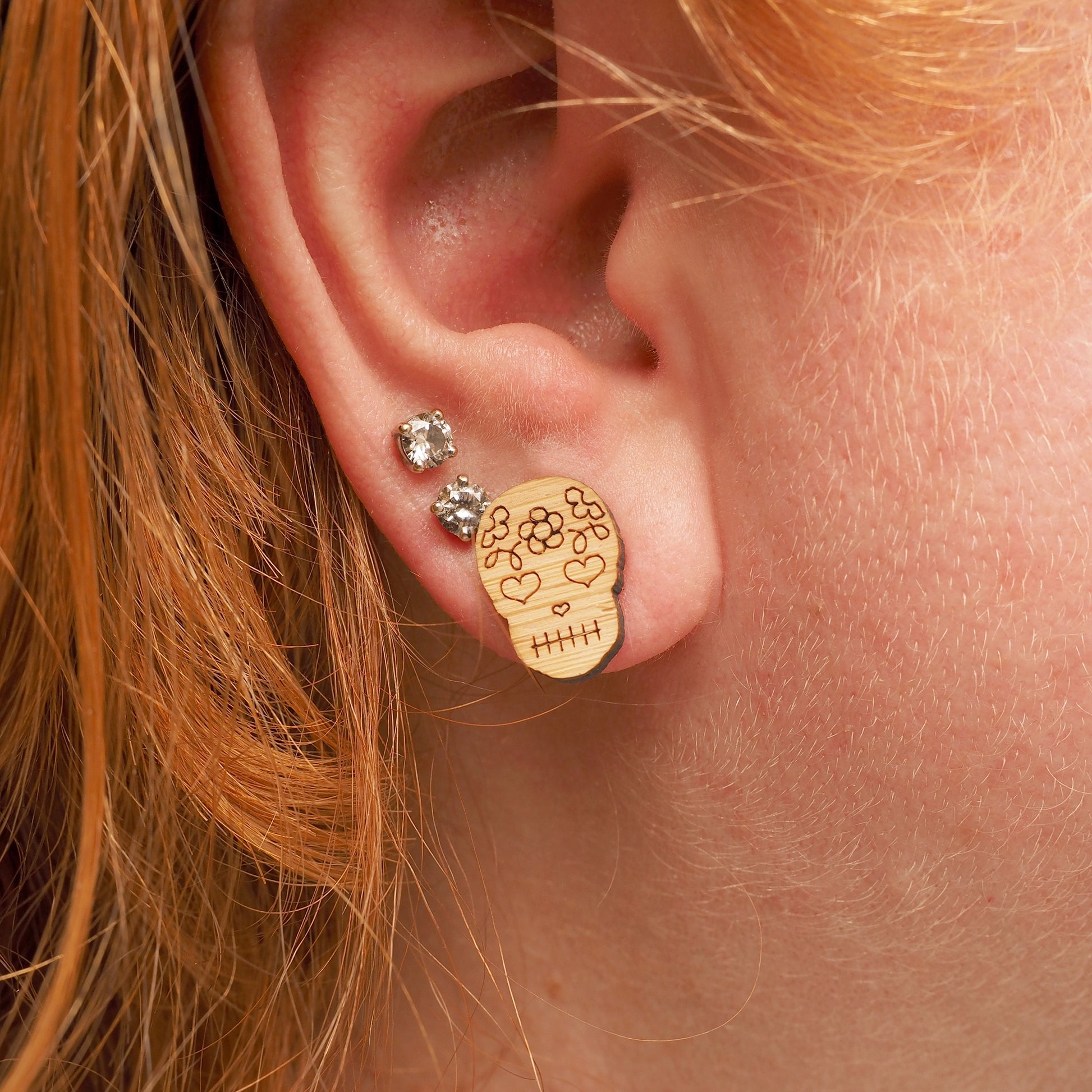 A person with red hair wearing a bamboo, skull-shaped earring. The earrings represent the Mexican Day of The Dead festival.