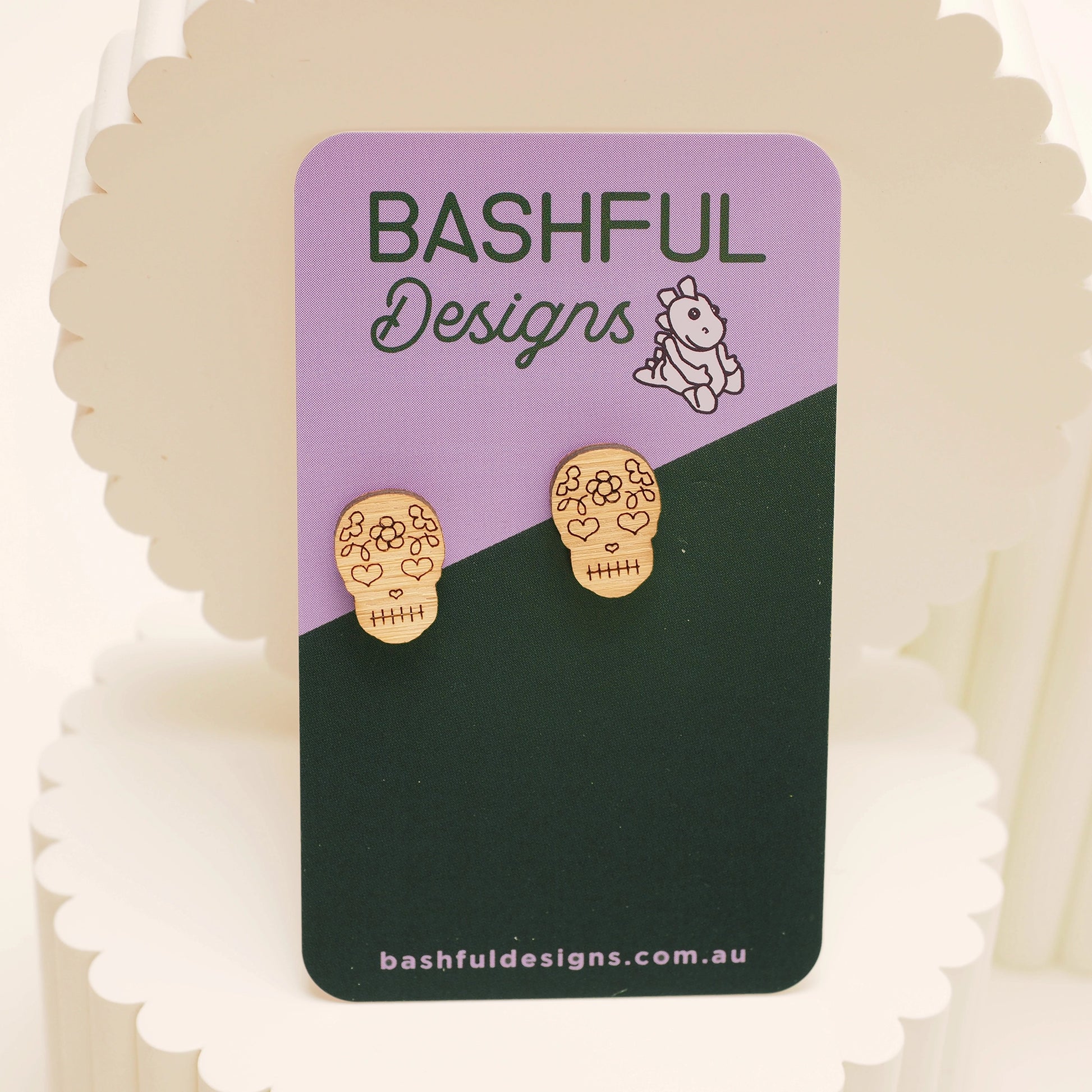 Bamboo, skull-shaped stud earrings that represent the Day of The Dead. These earrings are shown on a 'Bashful Designs' card.
