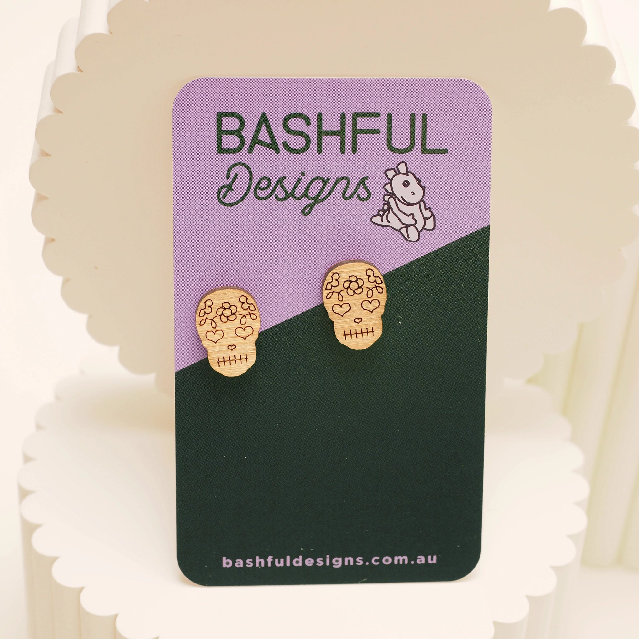 Bamboo, skull-shaped stud earrings that represent the Day of The Dead. These earrings are shown on a 'Bashful Designs' card.