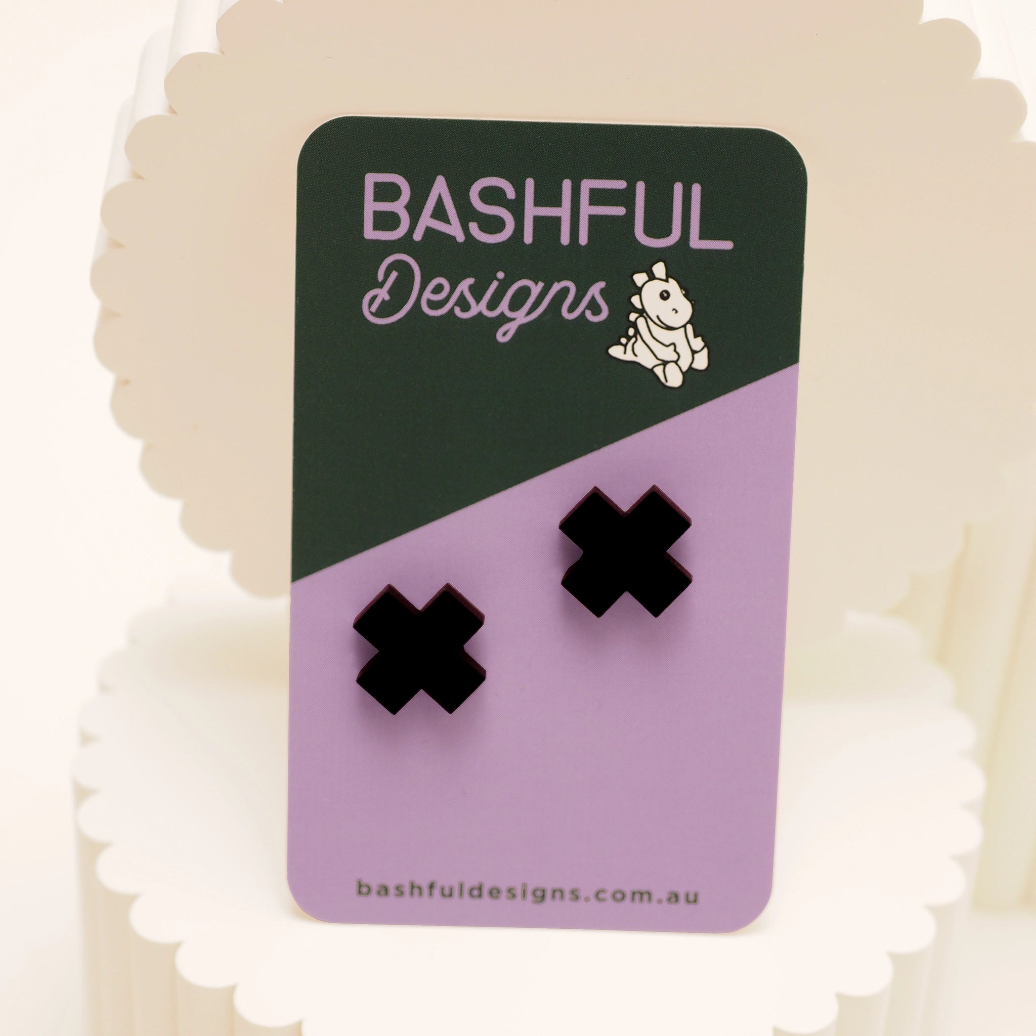 Black glossy stud earrings in the shape of the letter 'X'. The studs are shown on a 'Bashful Designs' branded card.