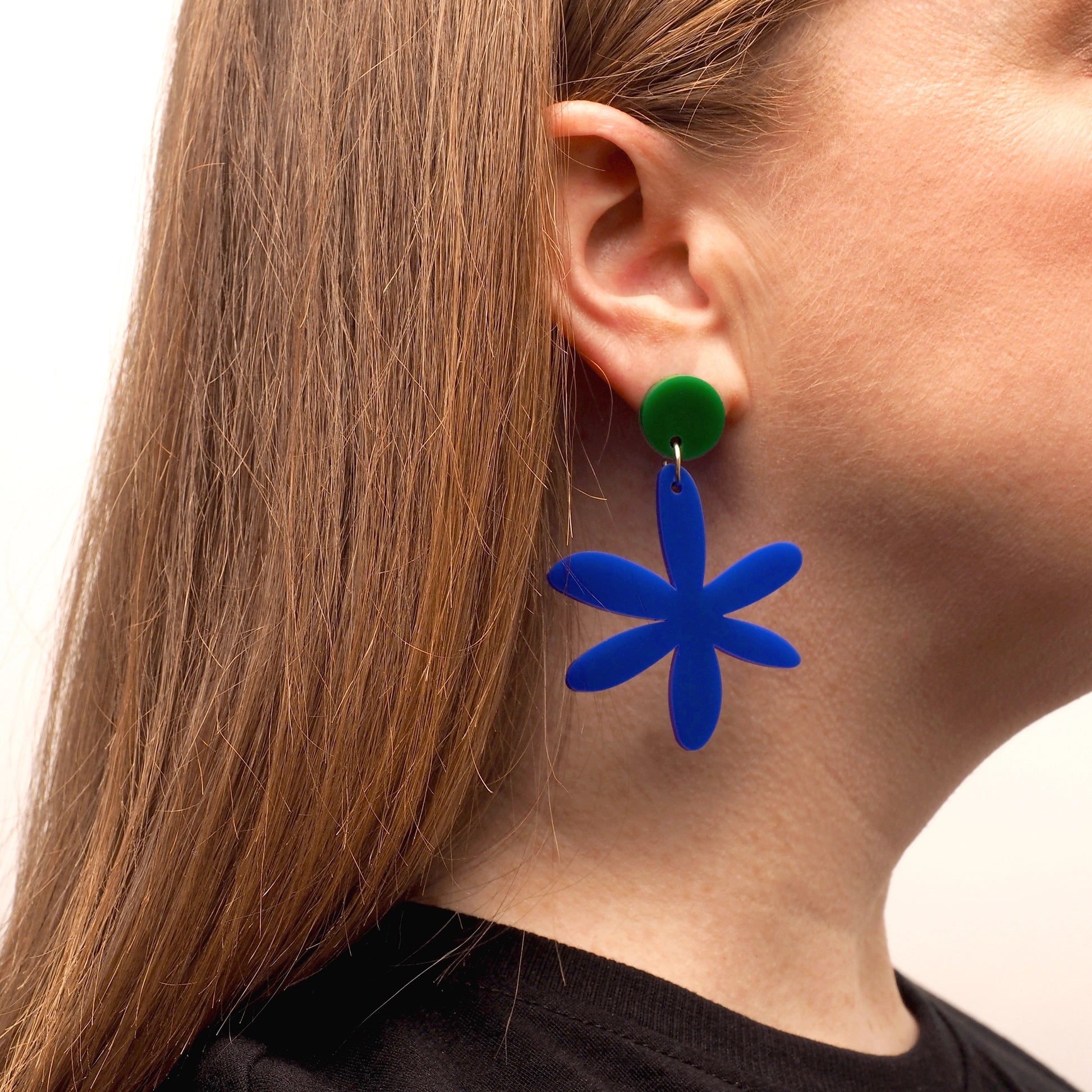 Navy blue acrylic, flower-shaped earring worn by a person with long red hair. These earrings are topped with a dark green round.