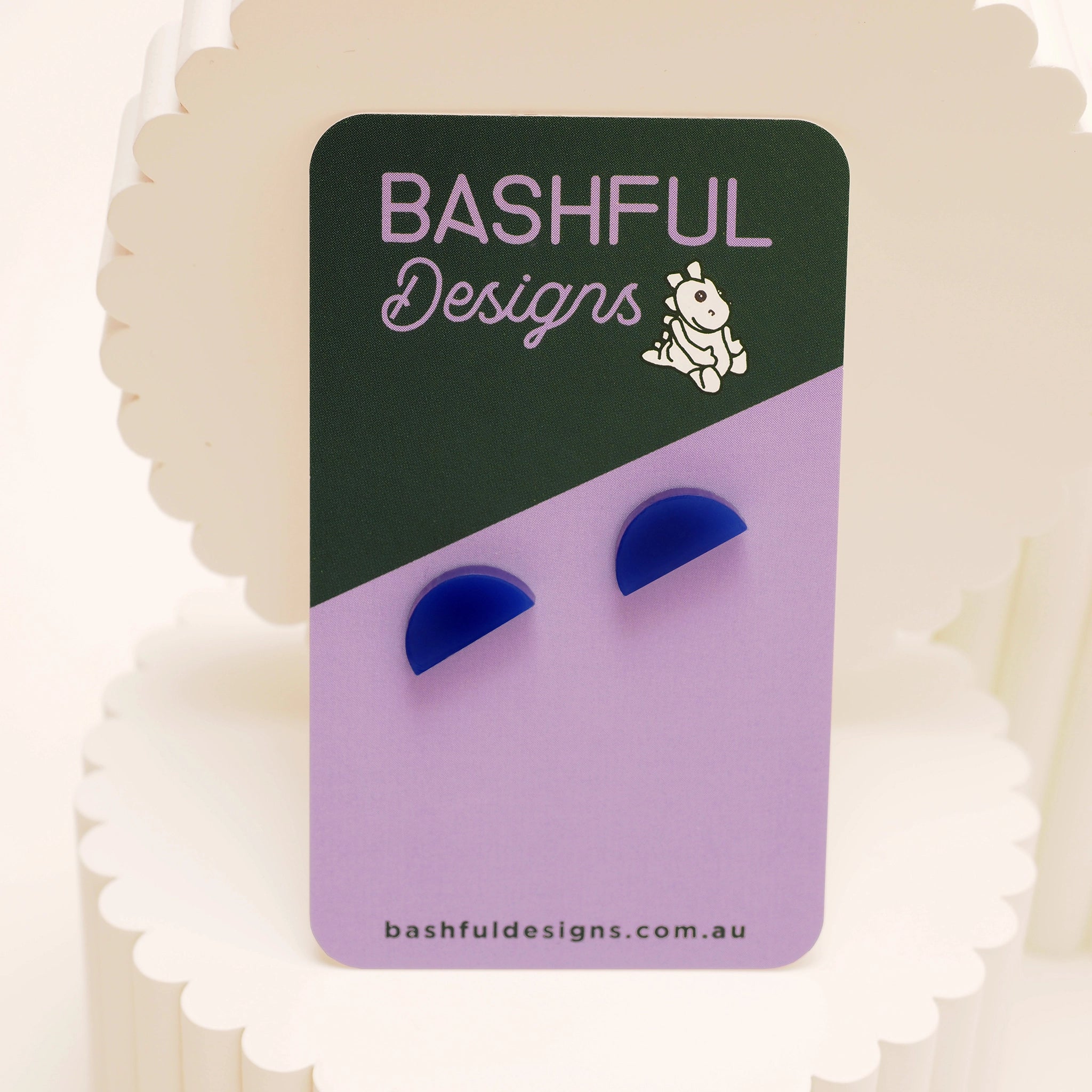 A pair of navy acrylic stud earrings in the shape of a half-moon. The earrings are shown on a 'Bashful Designs' branded card.