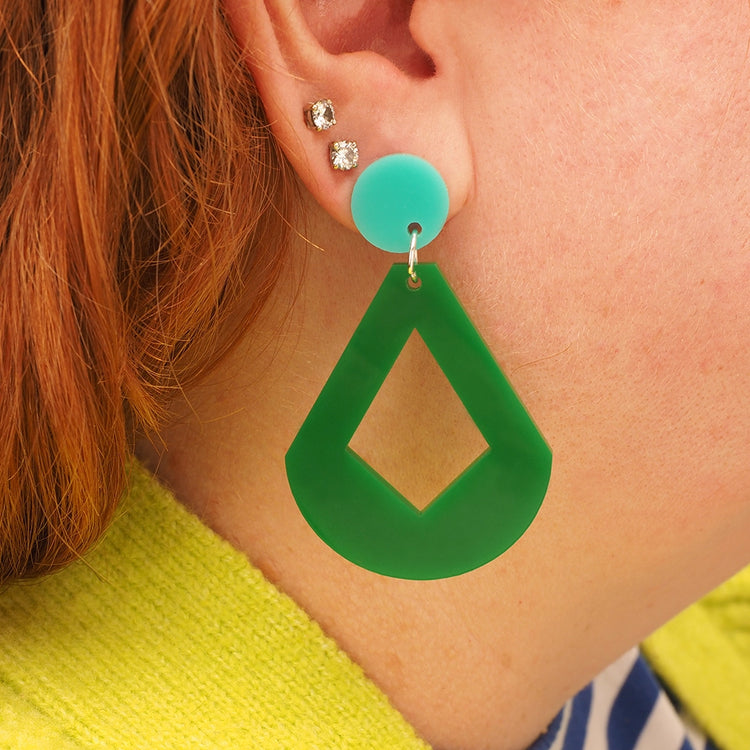 A side-on, profile view of our red headed model wearing the Green Diamond Drop dangle. The earring is made with an aqua round topper and a mid-green diamond shaped acrylic dangle.