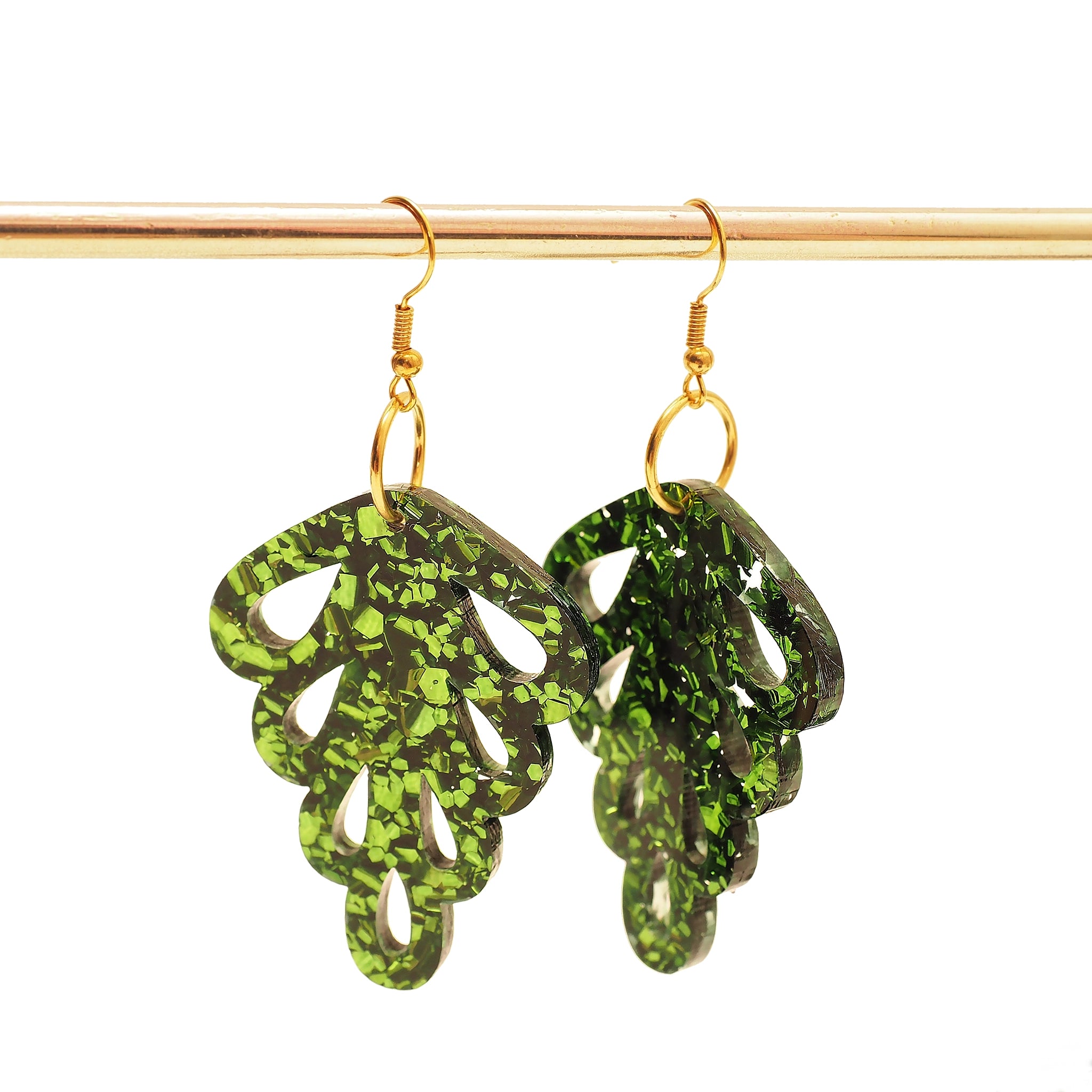 Green glitter acrylic earrings in the shape of a leaf. These earrings are hanging on a gold earring stand.