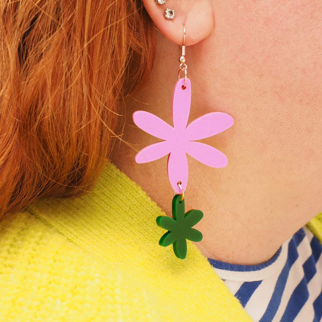 Pink and dark green acrylic flower earrings, worn by a person with long, curly red hair.