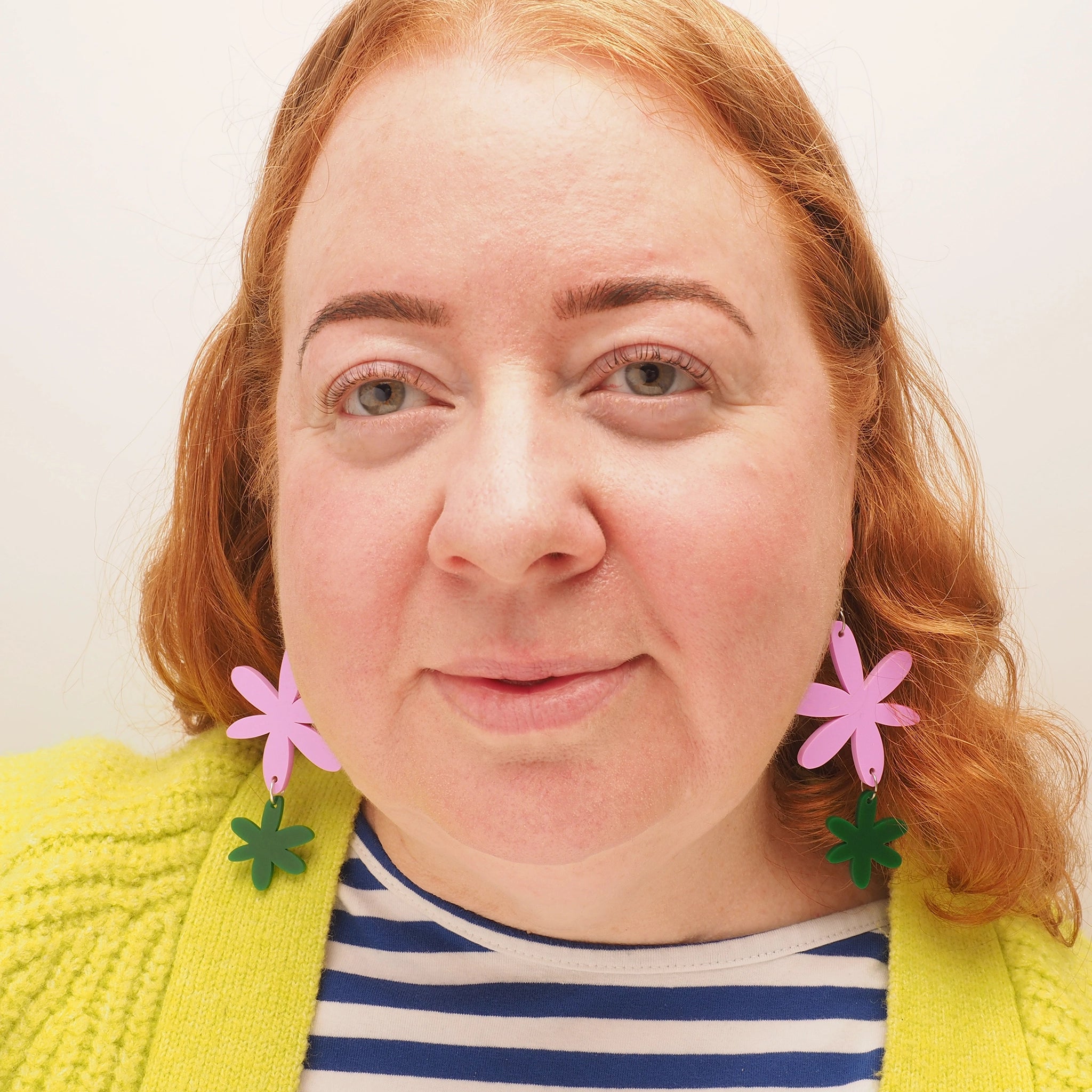 A curvy red-headed woman, wearing pink and green flower dangle earrings.