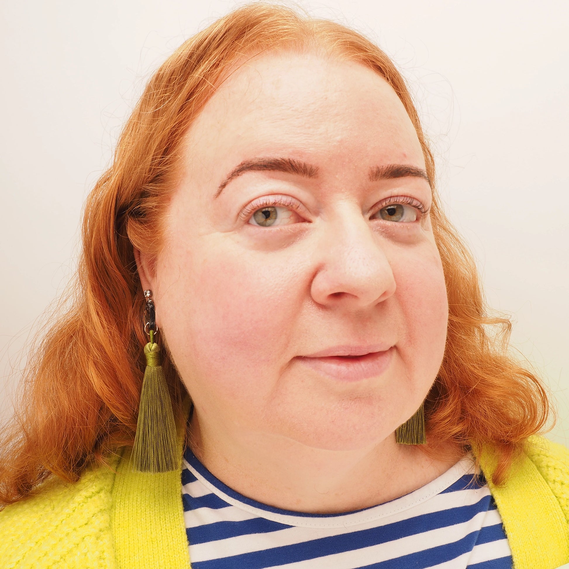 A curvy woman with red hair wearing a pair of long, dark green tassel earrings.
