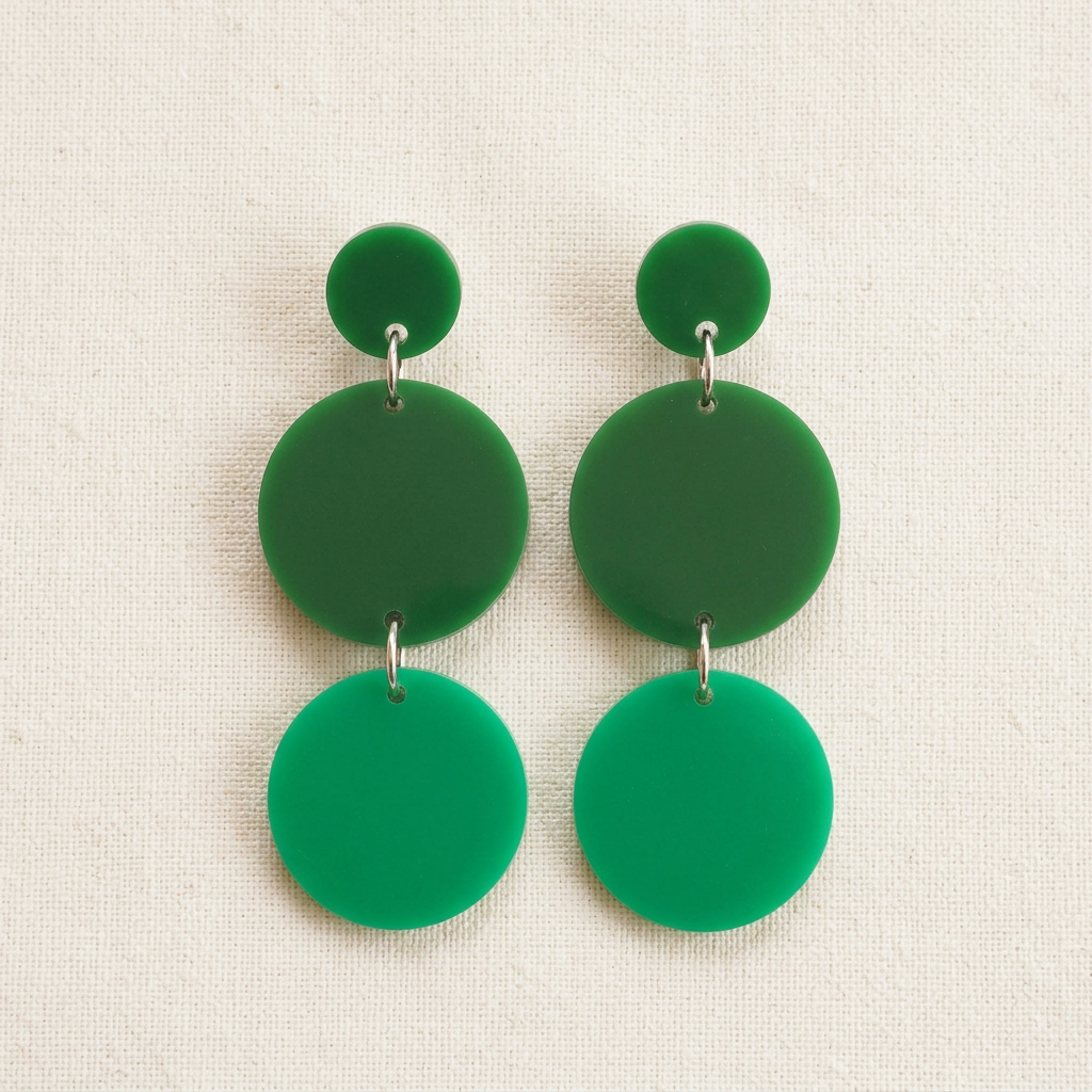 Flat lay of Emerald City earrings with three green acrylic circles linked by silver rings on a neutral background.