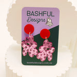 Pink acrylic balloon dog earrings that are shown on a 'Bashful Designs' card. These earrings are made from pink, mirrored acrylic, and engraved with polkadots.