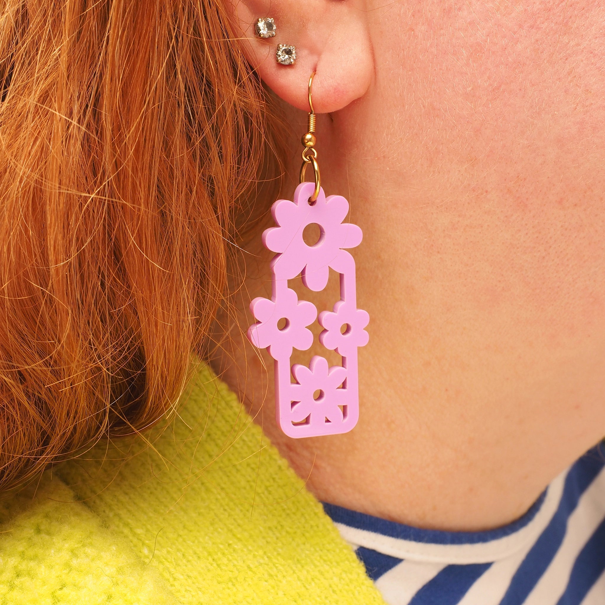 Pink floral acrylic dangle earrings worn by a person with red hair.