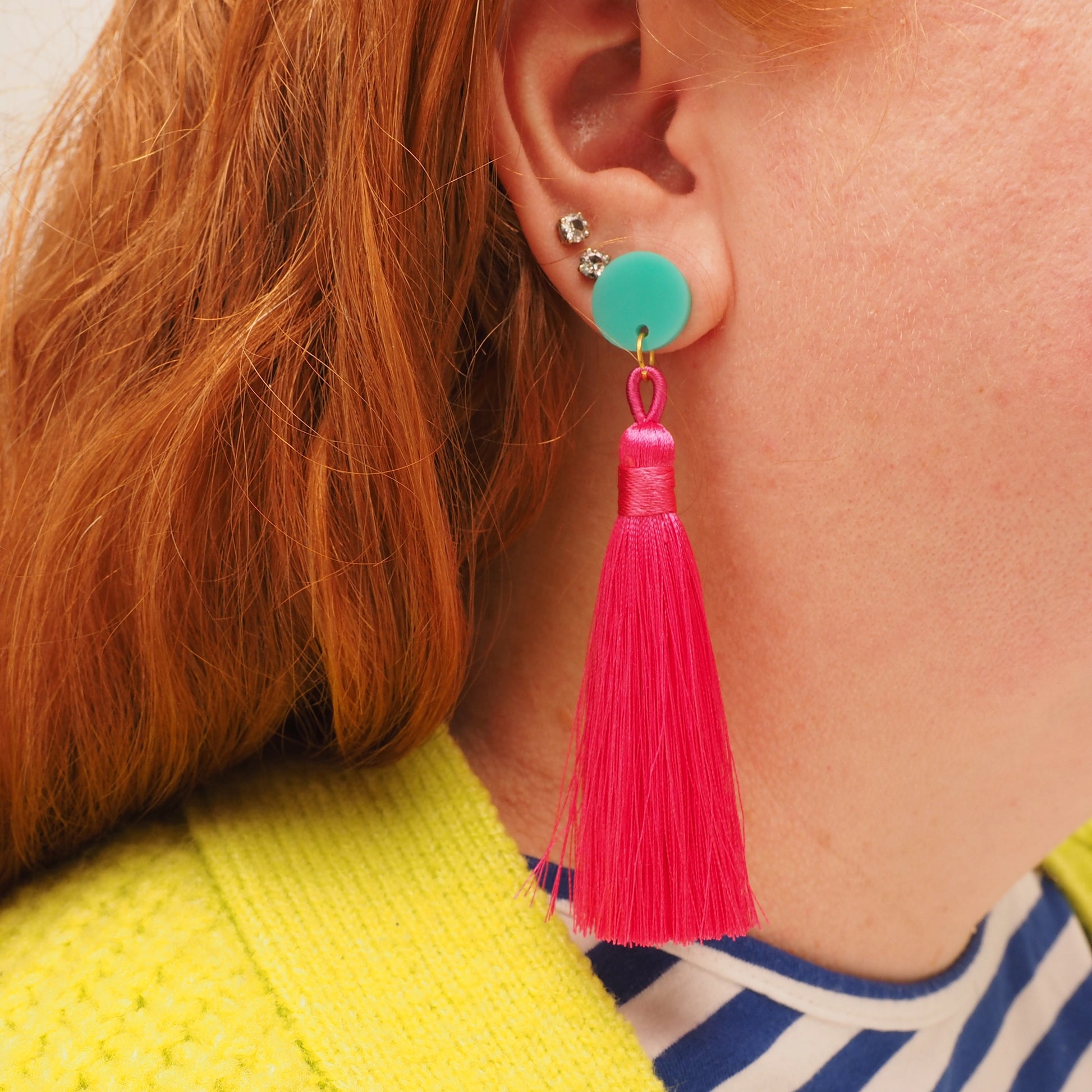 A person with long red hair, wearing a pair of bright pink tassel earrings.