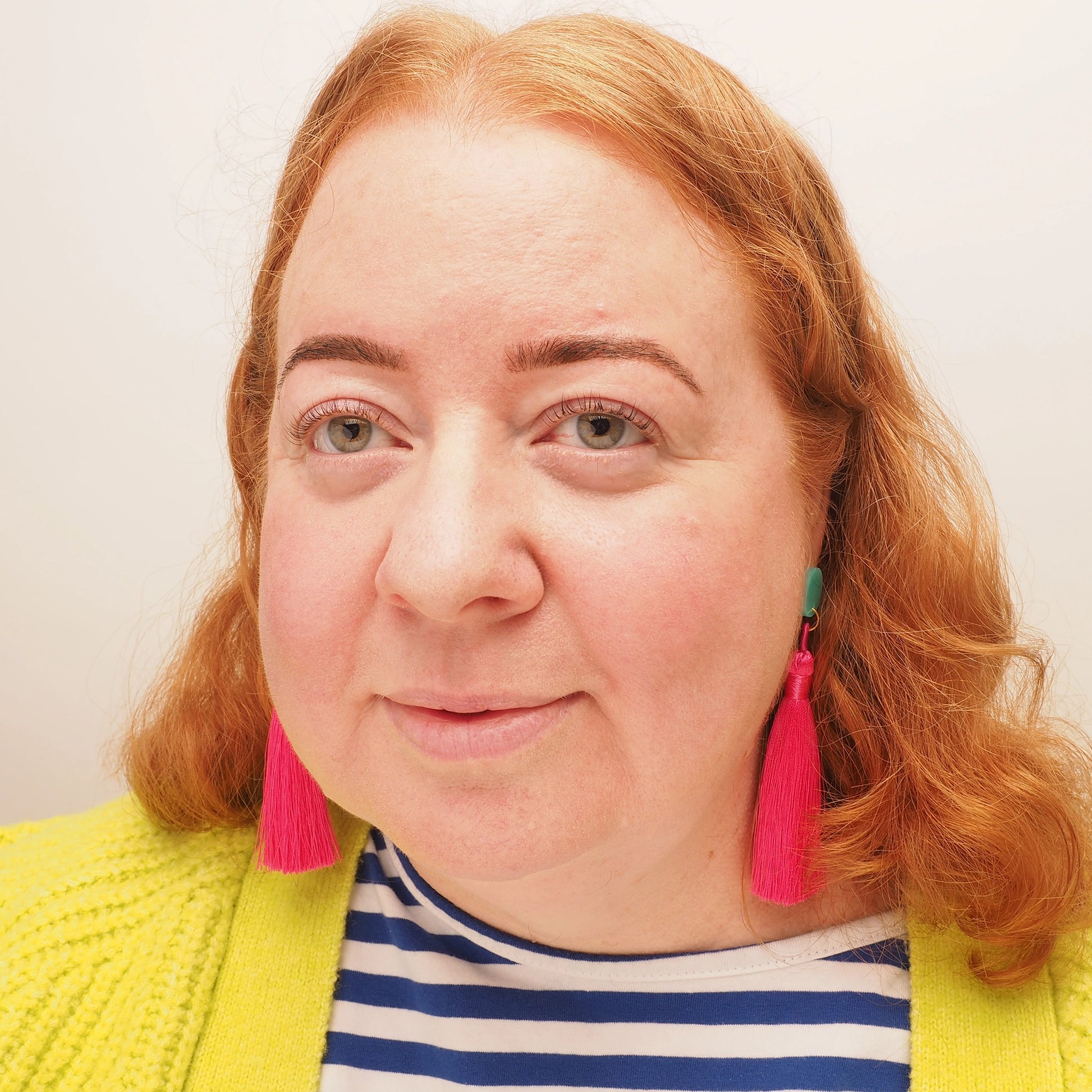 A curvy woman with red hair, wearing a pair of bright pink tassel earrings.