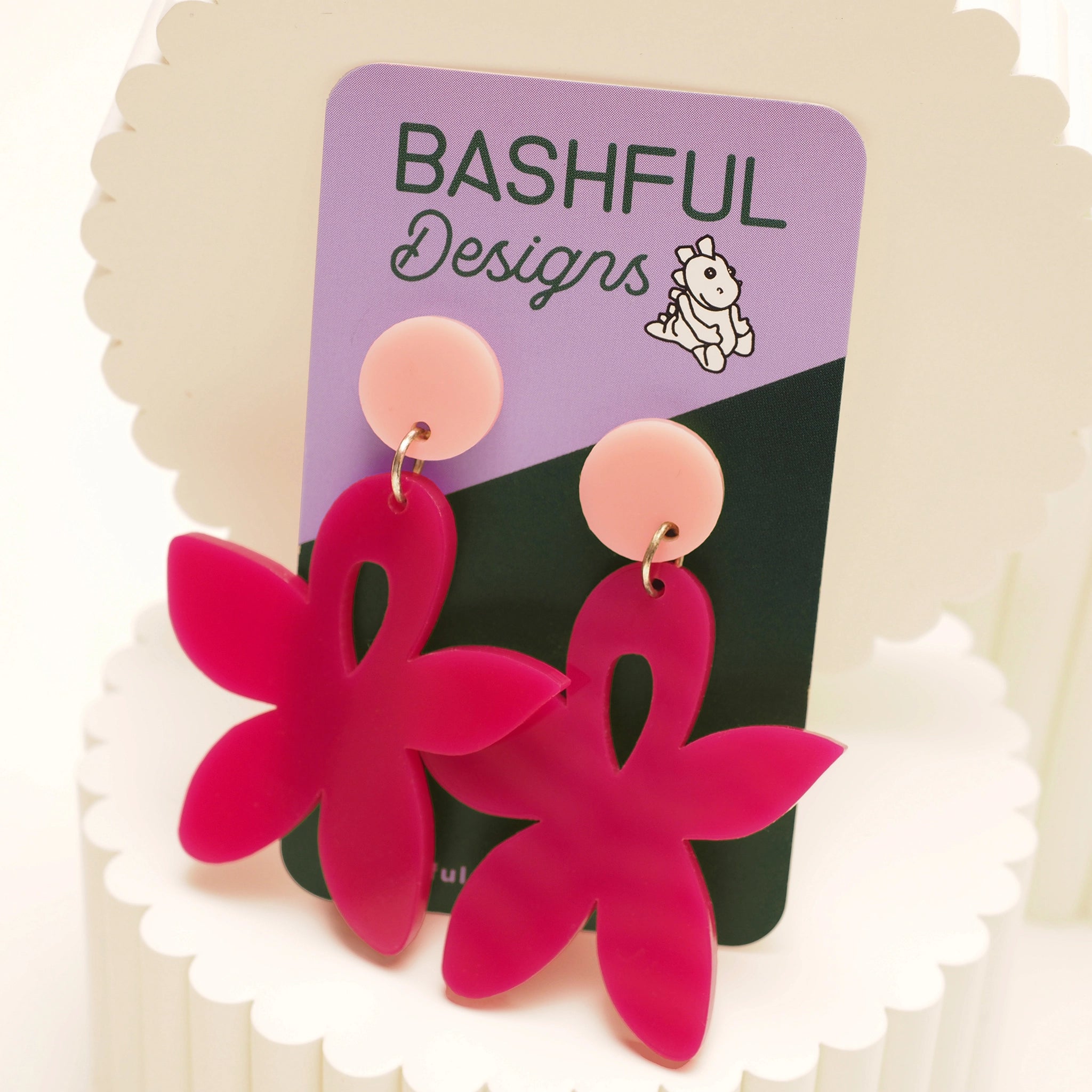 Bright pink acrylic floral earrings, with a light pink round topper on a 'Bashful Designs' branded card.