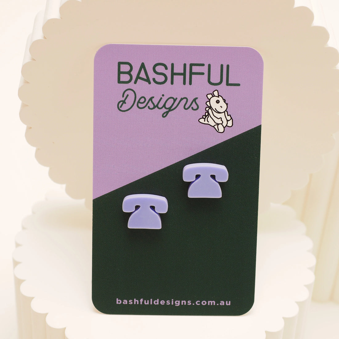 Light purple stud earrings in the shape of a telephone, on a 'Bashful Designs' card.