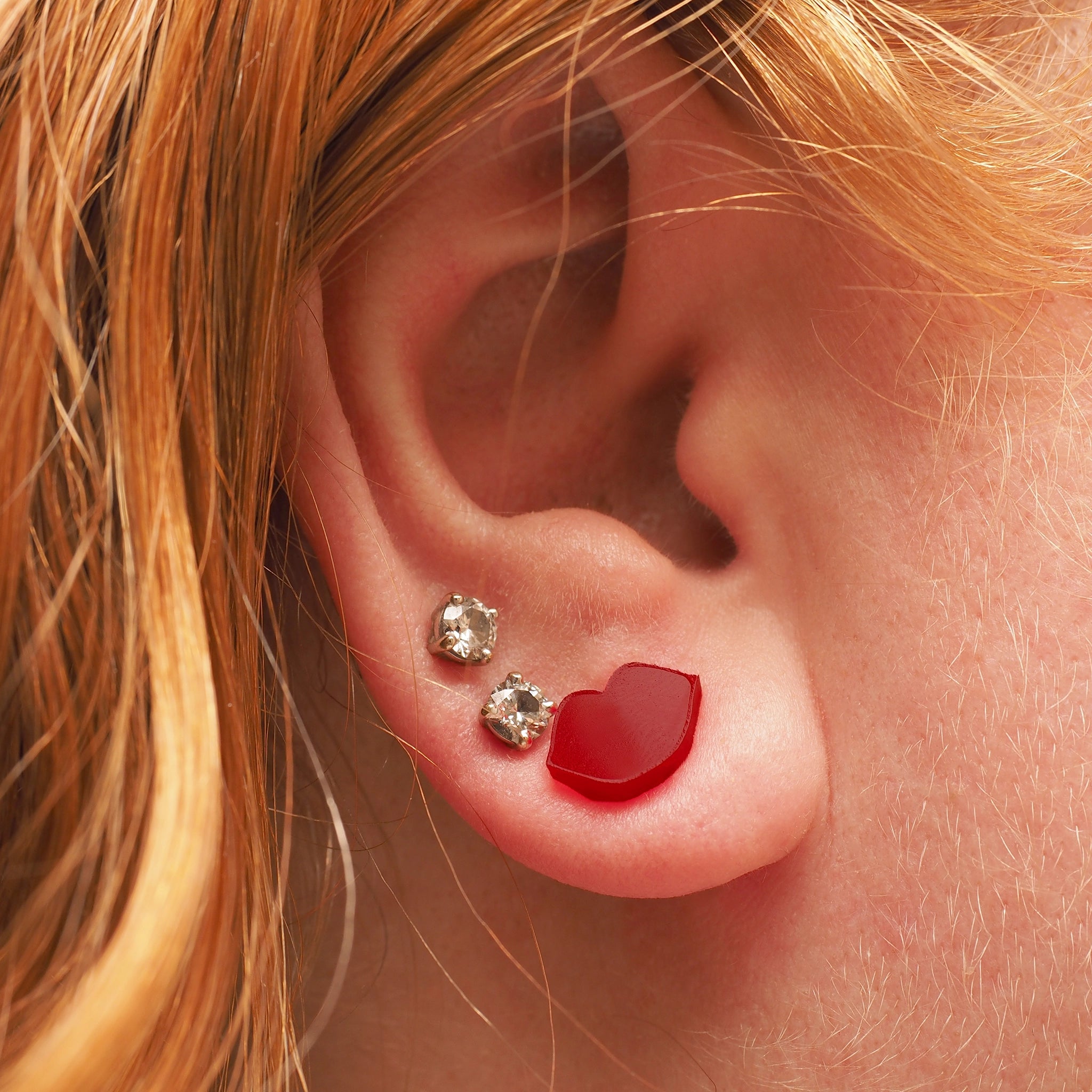 A red headed woman wearing small stud earrings in the shape of red lips.