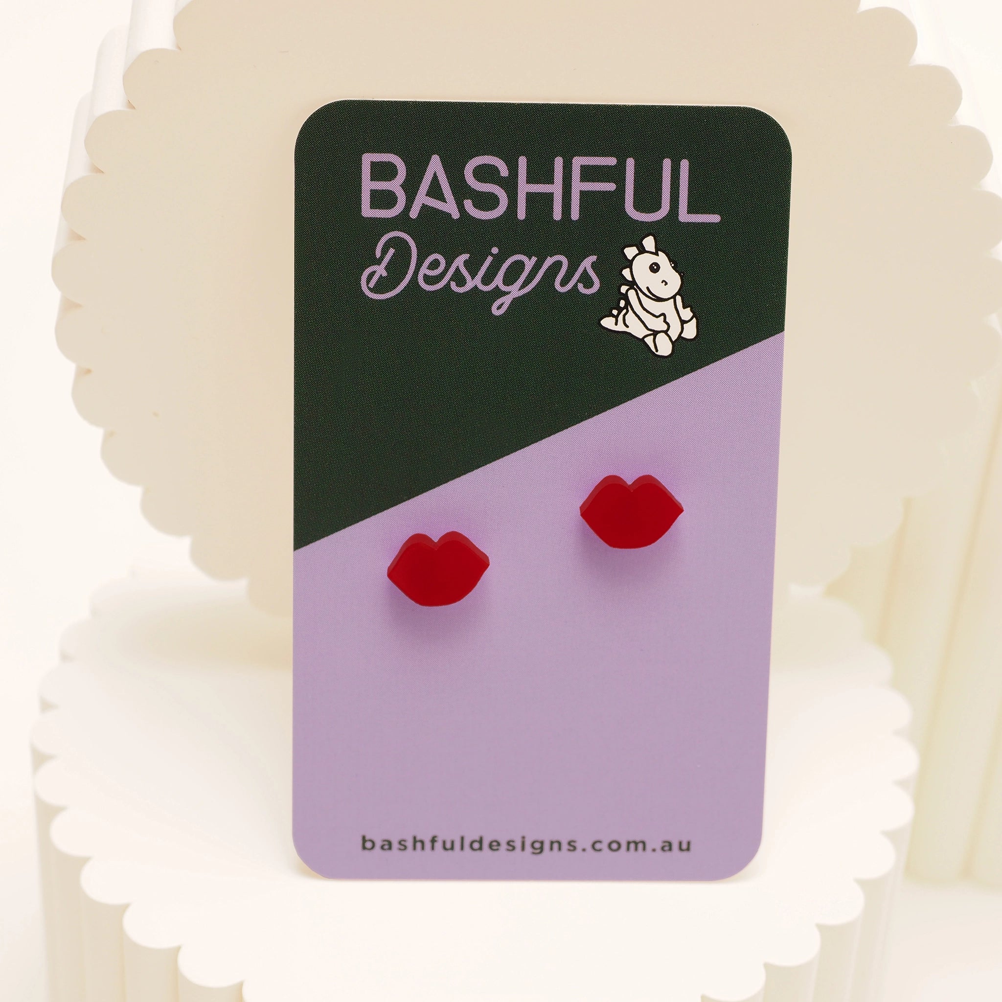 Red, lip-shaped stud earrings on a 'Bashful Designs' card.