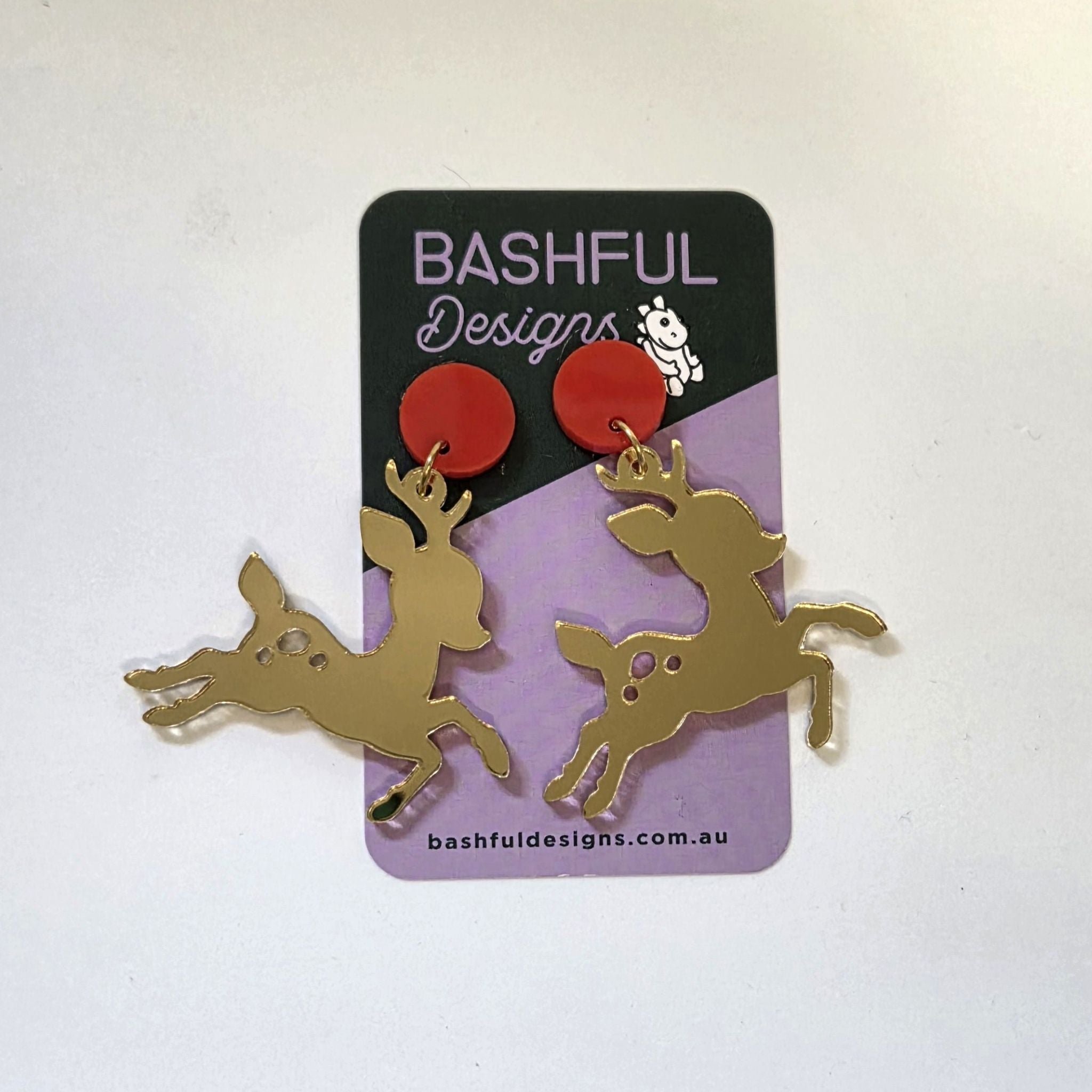 Earrings in the shape of reindeers, made out of gold mirror acrylic.  They are hanging from red circle acrylic toppers.