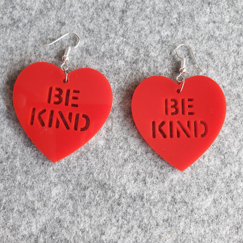 Red Be Kind Heart Earrings, facing front on to the viewer, on a grey felt background. These earrings are made from a red solid acrylic, with the words 