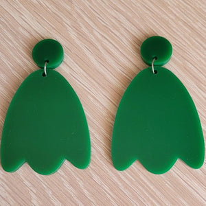 The Green Tulip Earrings begin with a solid round green acrylic stud, and continue to a solid green acrylic tulip shape.  The earrings are sitting on a wooden table.